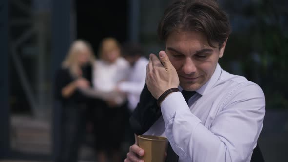 Young Handsome Man Rubbing Eyes Standing Outdoors with Disposable Cup Drinking Coffee in Slow Motion