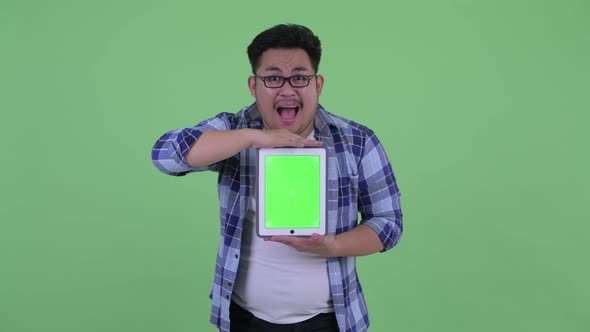 Happy Young Overweight Asian Hipster Man Showing Digital Tablet and Looking Surprised