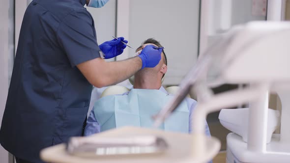 Adult Male Patient in Dentist Chair with Lip Retractor As Professional Orthodontist Examining Oral