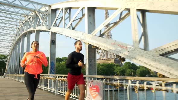 A man woman couple running across a bridge with the Eiffel Tower