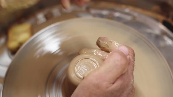 Potter Holds Clay on Spinning Potter's Wheel Wetting It with Water and Shaping Closeup