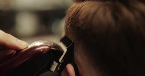 The Barber Makes a Haircut in the Barbershop with a Hair Clipper