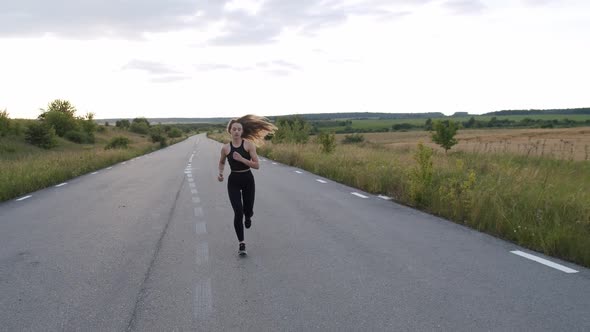 Young Sporty Girl with Long Hair Jogging on Road at Beautiful Nature