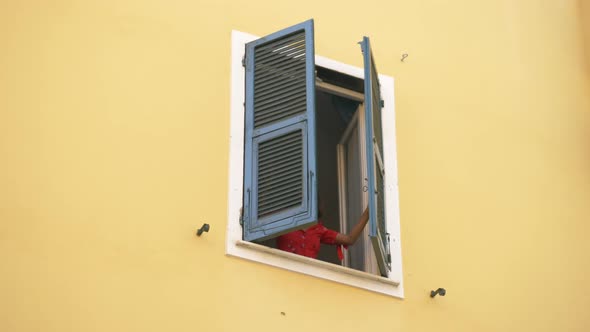 A woman opens shutters on a window traveling in a luxury resort town in Italy, Europe