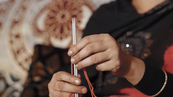 Indian woman knitting the first row with red thread and two needle crafts. Close up of knit work tie