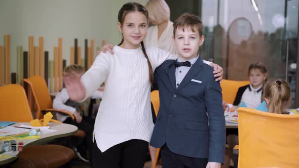 Beautiful Girl and Handsome Boy Hugging and Waving at Camera in Classroom