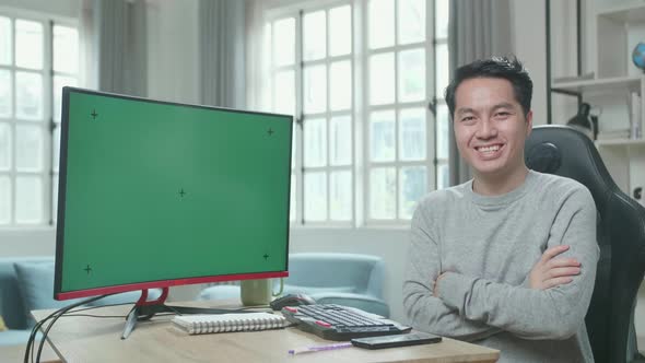 Asian Man With Green Screen Computer Crossing His Arms And Smiling To Camera While Working At Home