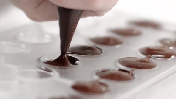 Hocolatier Hand with Pastry Bag Pouring Melted Dark Chocolate Into Mold Slow Mo