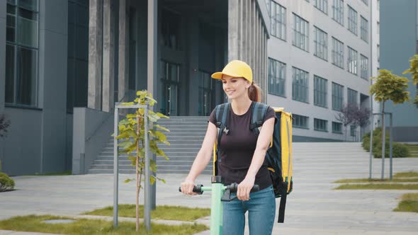 Smiling Young Delivery Woman Riding Scooter and Hurrying to Deliver Hot Food to