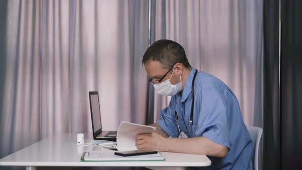 Tired Doctor in Uniform Reads Medical Records at Table