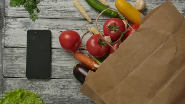 Vegetables Spinning Near Smartphone and Groceries. Vegetarian Concept.