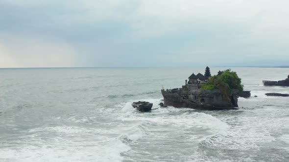 Aerial Dolly Shot Closing in on Tanah Lot Temple on a Dark Rocky Cliff in Rough Ocean with Large