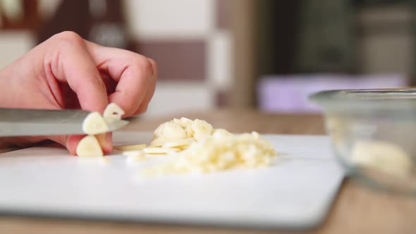 Girl Cuts Garlic with a Knife on the Board