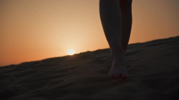 Barefoot woman walking on the sand in the desert in the evening