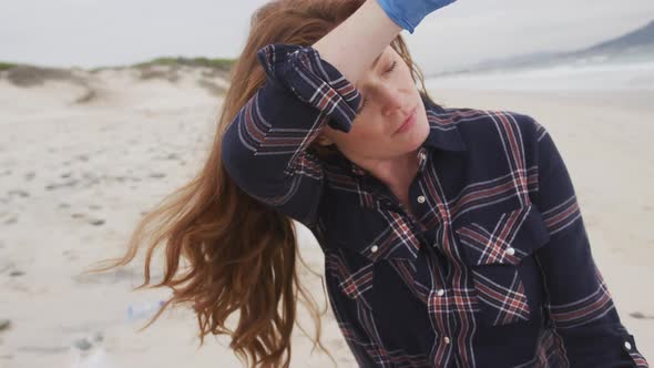 Caucasian woman wearing latex glove rubbing forehead looking toward sea and smiling