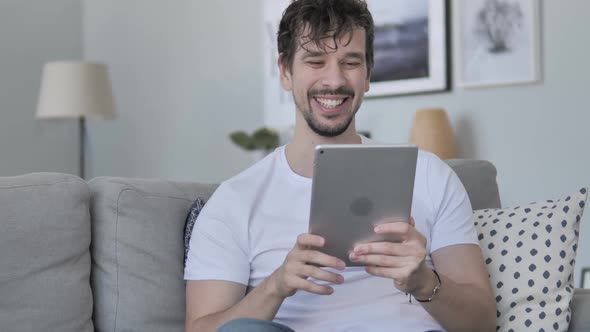 Online Video Chat on Tablet By Casual Young Man Relaxing on Couch