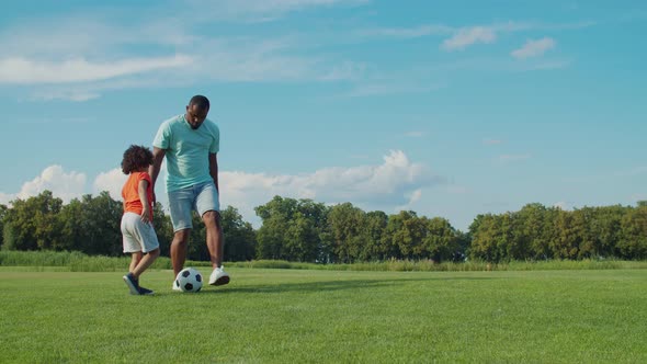 Father Teaching Little Boy To Play Soccer on Field