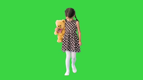 Shy Little Girl in Polka Dot Dress Hugging Her Teddy Bear While Walking and Looking Down at Her Feet