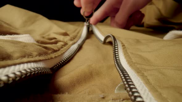 A Man Fastens a Metal Zipper on a Beige Jacket in Macro