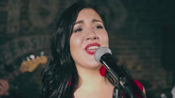 Young Attractive Girl Singing Into Microphone on Stage with Musicians