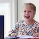 A little girl sits behind a laptop wearing headphones and laughs. - VideoHive Item for Sale