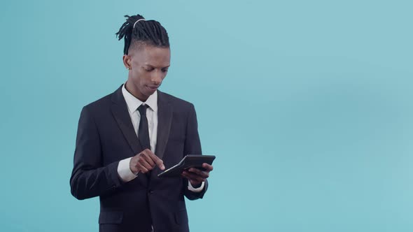 Black Man with Dreadlocks in an Official Suit Counts on a Calculator and Marvels at the Results