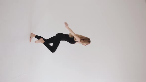 Charming Young Girl in a Black Top and Leggings Makes a Ballet Attitude Jump in the Studio on a