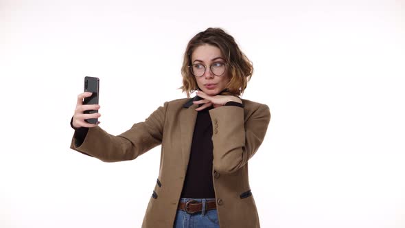 Gorgeous Young Woman in Brown Jacket Prapering Herself Looking to Her Smartphone and Taking a Selfie