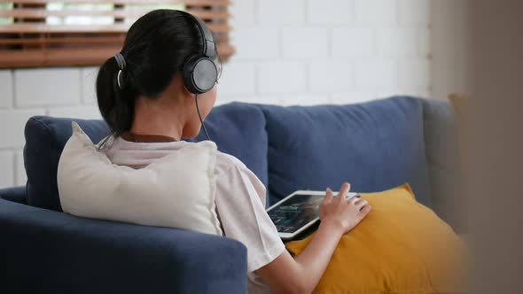 Portrait a beautiful young Asian woman while on a sofa in headphones listening music.