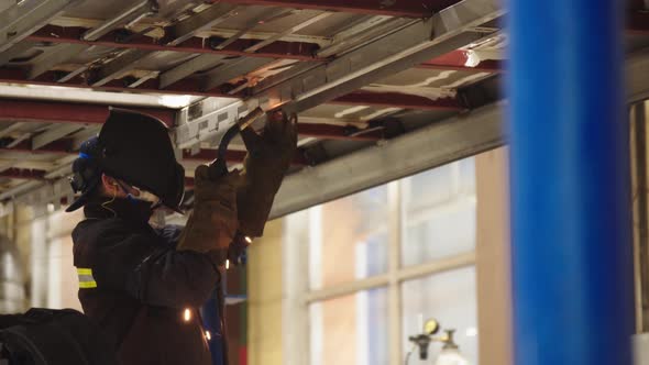 Closeup of Factory Worker in Protective Uniform and Safety Mask Welding Steel Structures for Train