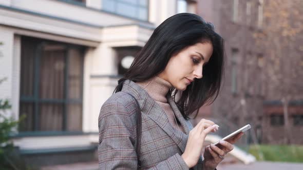 Portrait of a Confident Business Woman in a Suit Uses a Smartphone Outdoors