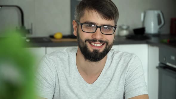 Man Drinks Cup of Fresh Coffee Looks at Camera and Smiles at Home in Kitchen