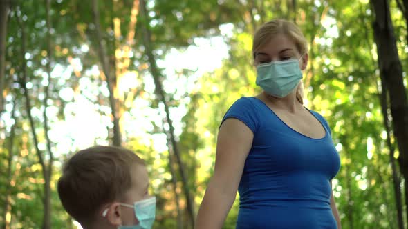 Mother and Child in Medical Masks Walk in the Park