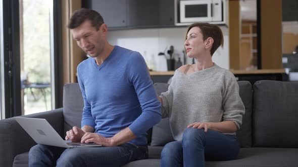 Busy Concentrated Man Messaging Online Ignoring Woman Sitting Down on Couch in Living Room