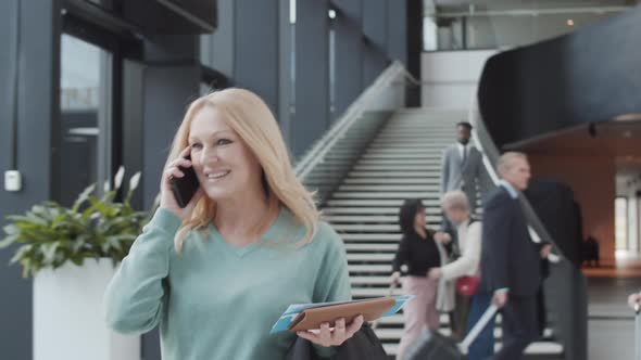 Blonde Lady with Boarding Pass Walking through Airport and Talking on Phone