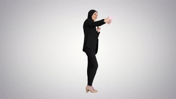 Smiling Arab Woman in Hijab Taking Selfie Pictures on Her Mobile Phone on Gradient Background