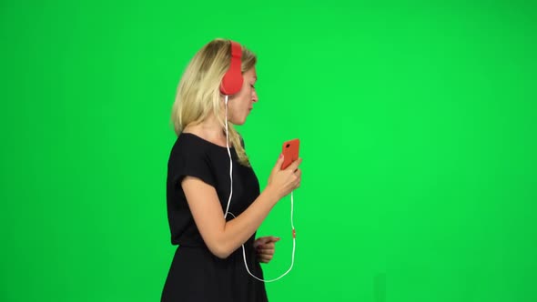 Cheerful Woman Walks in Big Red Headphones and with a Smartphone, Switches Music and Dancing