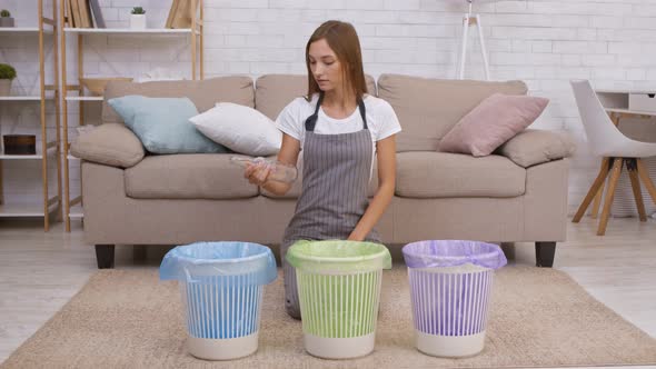 Young Positive Housewife Putting Glass Bottle Into Blue Dustbin at Home Supporting Environment