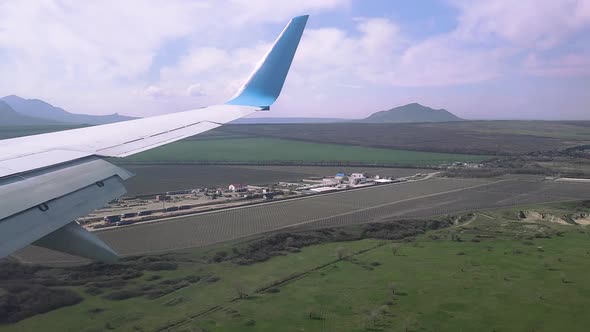 View of the Wing of a Flying Plane in Sunny Weather Over Fields Mountains and Settlements