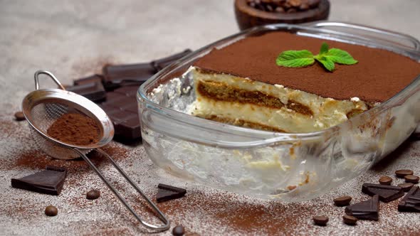 Traditional Italian Tiramisu dessert in glass baking dish on grey concrete background