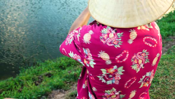 Young mysterious man with conical hat and exotic shirt fishing in local pond, close up view