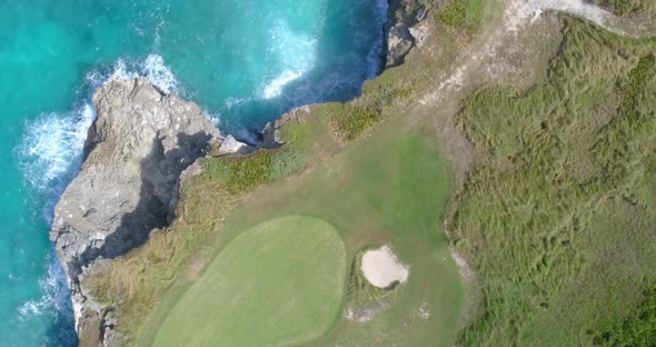 Top down view of rocky coastline, turquoise clear ocean water and green golf course greens with sand