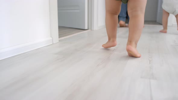 Legs of Unrecognizable Triplet Toddlers Walking at Home with Mom alt