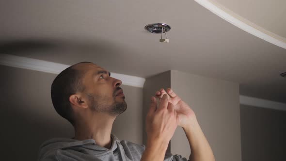 Young Man Repairing Cable Wiring and Installs or Replaces the Halogen Lamp on the Ceiling