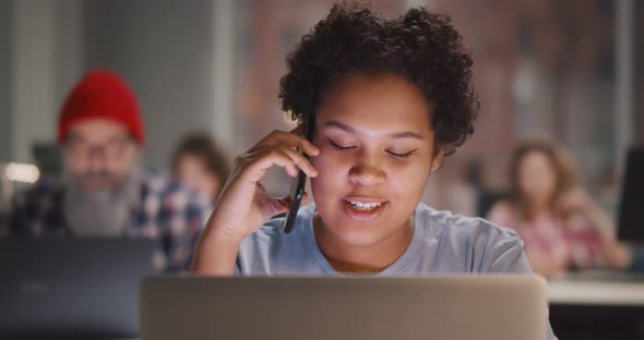 African American Woman Is Talking on Phone and Using Laptop Computer at Contemporary Office