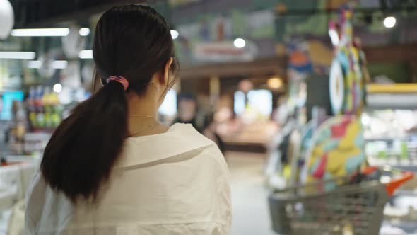 Busy Woman Walks Past Racks Searching Goods in Supermarket