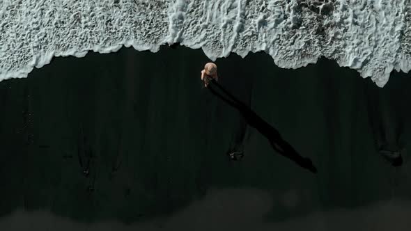 Breathtaking Aerial View of a Stylish and Free Woman with a Hat and Dress on a Black Volcanic Sand