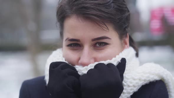 Close-up of Young Brunette Caucasian Girl with Brown Eyes Hiding Face in White Warm Scarf. Portrait