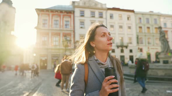 Woman with a Thermos Cup in Hand Walking Down the Street and Admires the Architecture of the Old