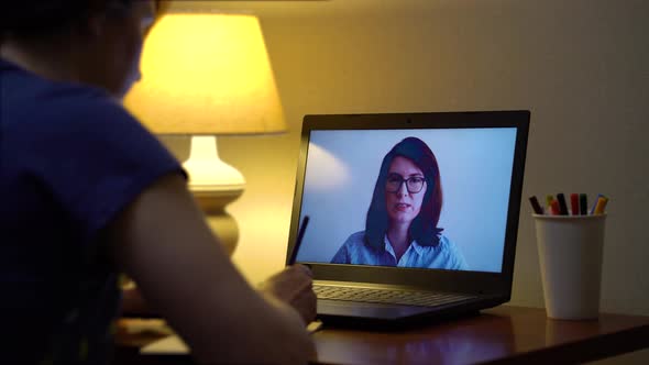 Young woman watching online course on laptop at home in the evening